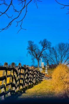 a wooden fence in the middle of a grassy field with trees and tombstones behind it