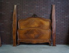 a wooden bed sitting in front of a brick wall next to two tall wooden poles