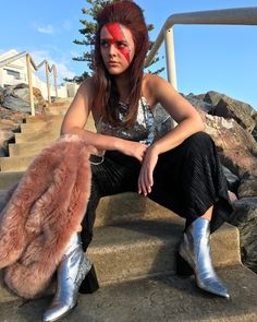 a woman with red hair sitting on some steps wearing silver boots and a fur coat