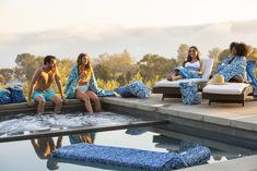 four people sitting on lounge chairs next to a pool