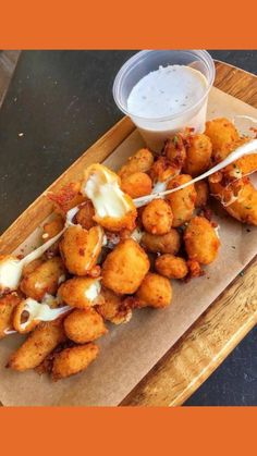 some fried food is sitting on a wooden platter with a small container of ranch dressing