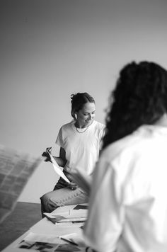 two women sitting at a table with books and papers in front of them, one holding a piece of paper