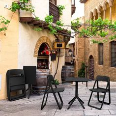 three chairs and two tables sitting in an alleyway next to a building with vines growing on it