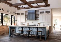 a large kitchen with an island and bar stools in the center, surrounded by wooden flooring