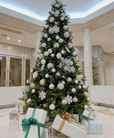 a christmas tree with presents under it in the middle of a room filled with white and silver decorations