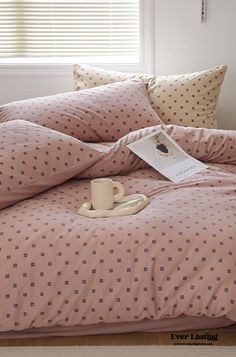 a coffee cup on a bed with pink sheets and pillow cases in front of a window