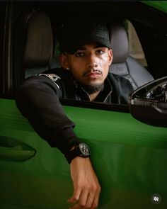 a man sitting in the driver's seat of a green car with his hand on the door handle