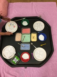 a child is painting on a tray with paints and paper plates in front of them