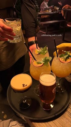 three glasses filled with drinks on top of a black plate next to another glass full of liquid