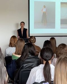 a woman standing in front of a group of people while giving a presentation on a projector screen