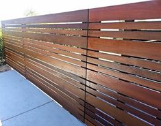 a wooden fence is shown in front of a sidewalk and shrubbery on the other side