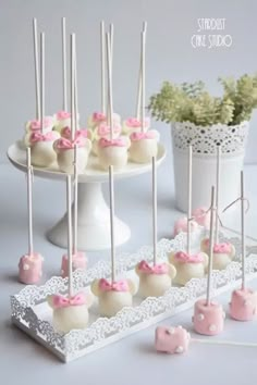 cake pops with pink bows on them are arranged on a white platter next to a potted plant