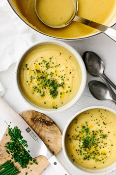 two white bowls filled with soup next to a cutting board and spoons on a table