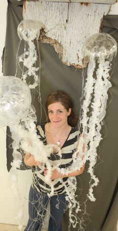 a woman standing in front of an art piece made out of plastic jellyfishs