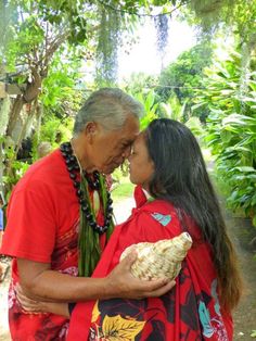 an older man and young woman sharing a kiss in front of some tropical trees,