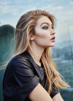 a woman with long blonde hair and blue eyes posing for a photo in front of a cityscape