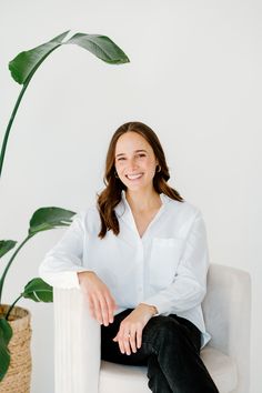 a woman sitting in a chair next to a potted plant and smiling at the camera