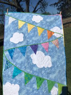 a quilt hanging on a clothesline with flags and clouds in the sky above it