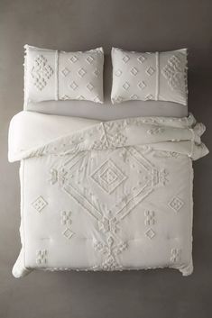 a white bed with two pillows on top of it and one pillow in the middle