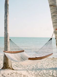 a hammock hanging between two palm trees on the beach