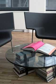 a glass table with books on it in front of two black chairs and one pink book