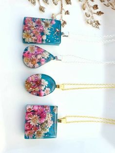 three necklaces with flowers on them sitting next to a gold chain and a glass pendant