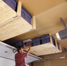 a man is working on the underside of a garage storage unit with blue bins