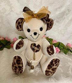 a white teddy bear with brown spots and a gold bow on it's head