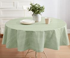 a green table cloth with a white plate and cup on it next to a potted plant