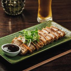 a green plate topped with meat next to a cup of sauce and chopsticks