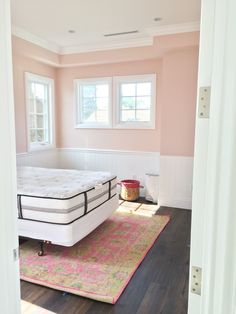 a bedroom with pink walls and wood floors has a white mattress on top of it