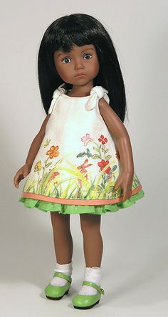 a doll with black hair wearing a white dress and green shoes, standing in front of a white background