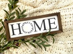 a sign that says home on it next to some leaves and branches in front of a white blanket