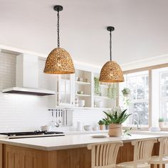 two lights hanging over a kitchen island with stools in front of it and a potted plant on the counter