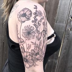 a woman's arm with flowers and leaves on it, in front of a wooden fence