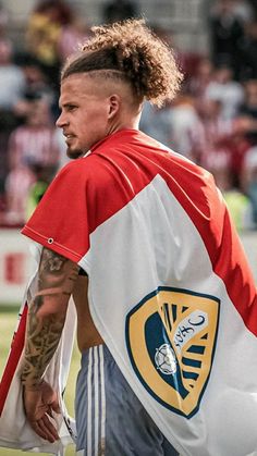 a man with long hair wearing a red and white shirt holding a bag in front of him