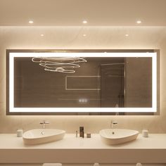 two white sinks in front of a large mirror with lights on it's sides