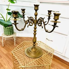 a metal candelabra with four candles on it sitting on a wooden floor next to a potted plant