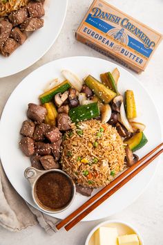 a plate with rice, meat and vegetables on it next to chopsticks and sauce