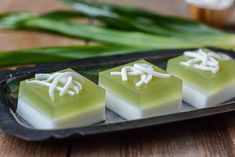 three pieces of soap sitting on top of a black tray next to green onions and leaves