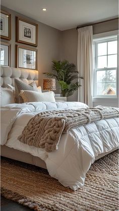 a large white bed sitting in a bedroom next to a window with pictures on the wall