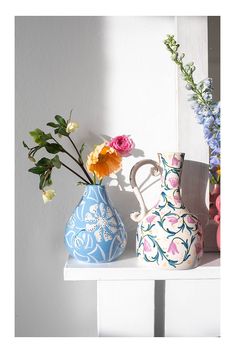 three vases with flowers in them sitting on a shelf