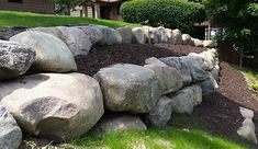 a pile of rocks sitting on top of a lush green hillside next to a house