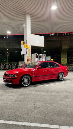 a red car is parked in front of a gas station with no one around it