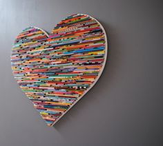 a heart made out of many different colored pencils on a gray wall with grey background