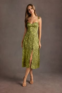 a woman in a green dress posing for the camera with her hand on her hip