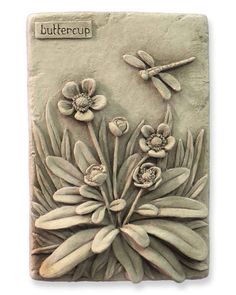 a stone plaque with flowers and dragonflies on it's face, in front of a white background