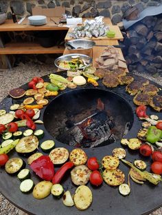 an outdoor grill with lots of vegetables and food cooking on the outside fire pit area