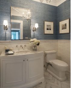 a white toilet sitting next to a sink in a bathroom under a vanity with two mirrors above it