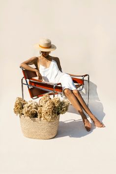 a woman sitting in a chair next to a basket with flowers on it and her legs crossed